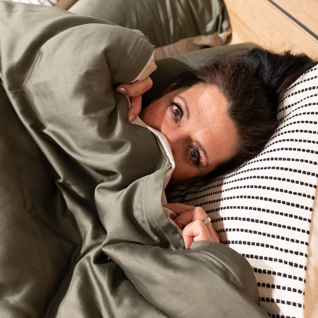 Nina kuschelt sich lächelnd in grüne Bettwäsche und vermittelt Geborgenheit und Wohlfühlmomente.